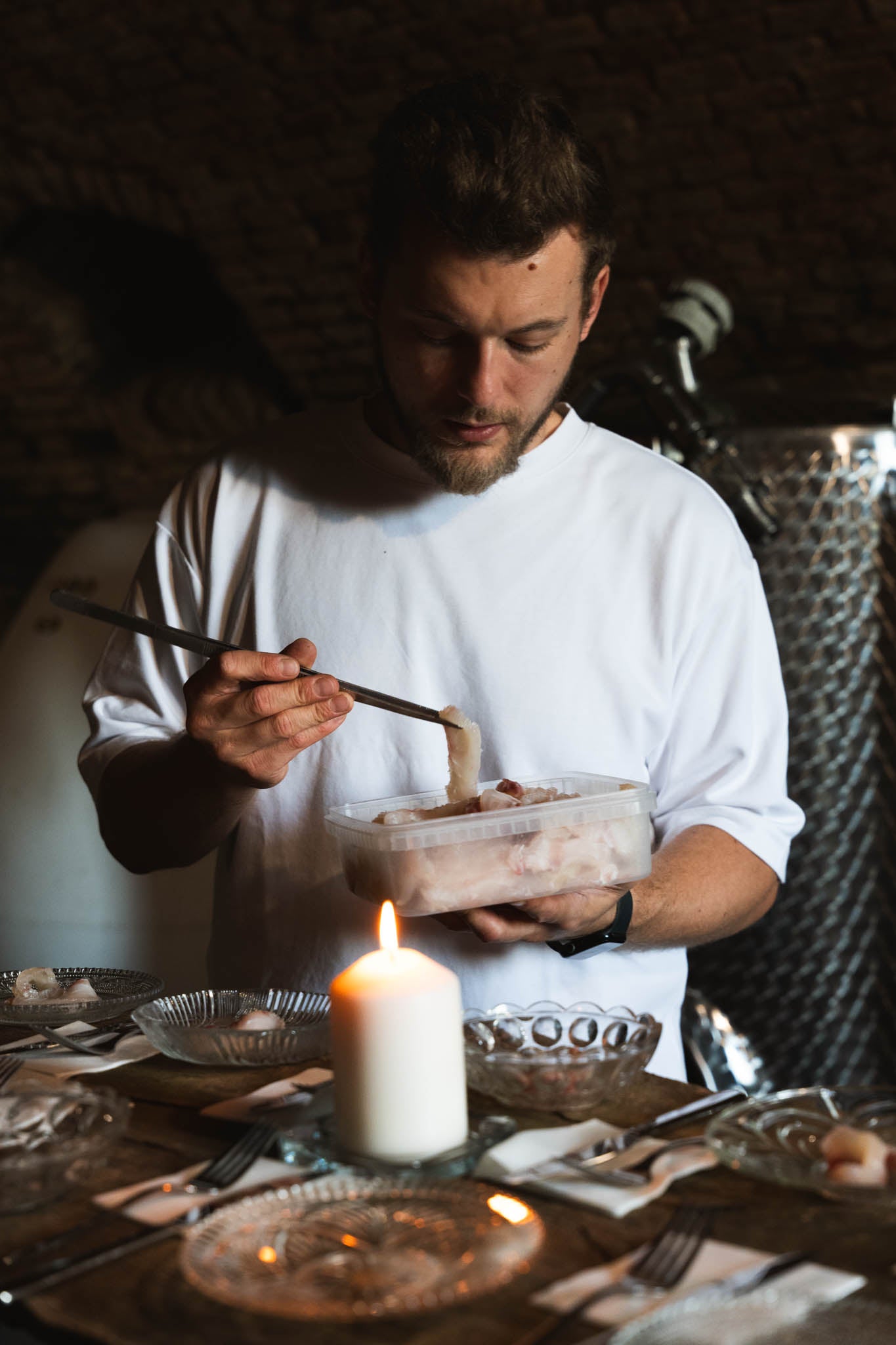 Chef preparing food for b-üzem event, at a dimly lit table with a candle.