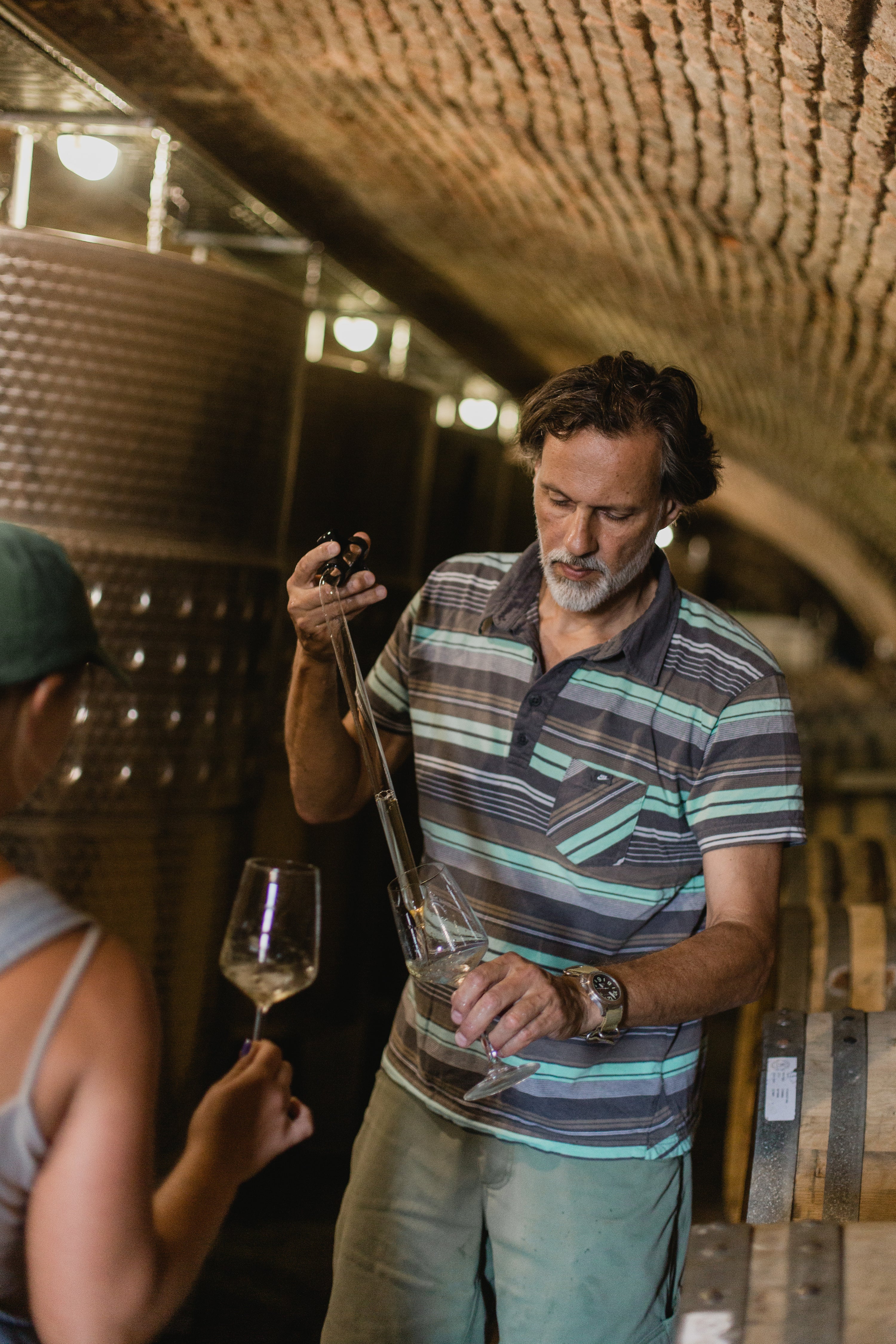 Robert Gilvesy in a striped shirt holding Gilvesy organic wine tasting in a winery setting.